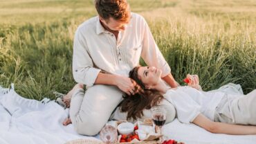 Pareja de recién casados con salud integral disfrutan de un picnic con copa de vino y frutas en el campo.
