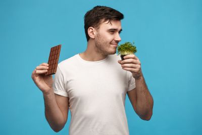 Joven muestra en una mano una barra de chocolate y en la otra está oliendo una verdura.