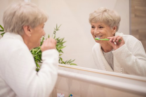 Mujer adulta mayor está cepillándose los dientes frente al espejo.