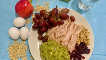 Un plato contiene uvas, jamon, aguacte, frutos secos más agua para hacer ayuno intermitente.