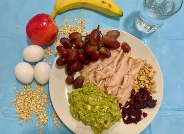 Un plato contiene uvas, jamon, aguacte, frutos secos más agua para hacer ayuno intermitente.