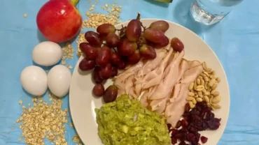 Un plato contiene uvas, jamon, aguacte, frutos secos más agua para hacer ayuno intermitente.