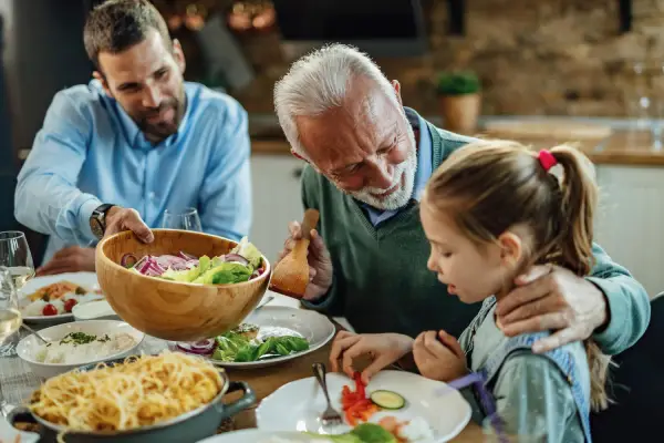 Un abuelo, su hijo y nieta están en la mesa conversando con calma. Un ejemplo de no caer en patrones que no son saludables.