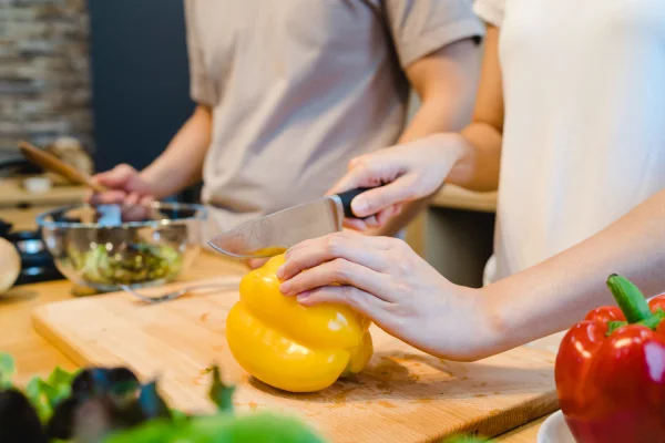 Manos de una mujer cortando un pimiento en una tabla de cocina, un ejemplo de nutrición consciente sobre cómo romper patrones familiares que enferman.