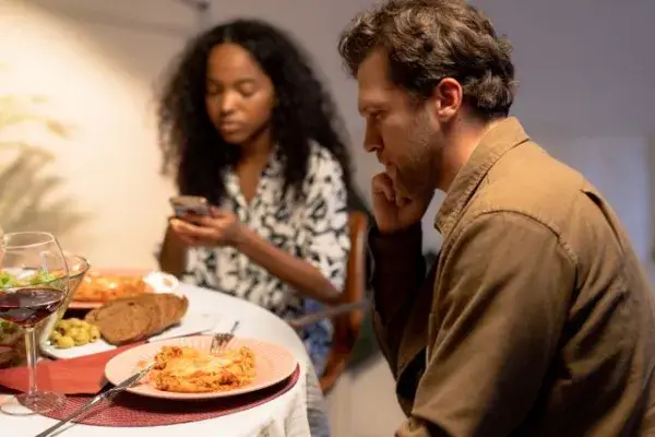 Mujer distraída con el teléfono celular ignorando a su pareja mientras están cenando.