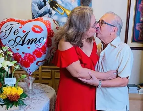 Carmen Zea y Amalio Martinez se están besando dulcemente junto a un globo de corazón que dice "Te Amo" .