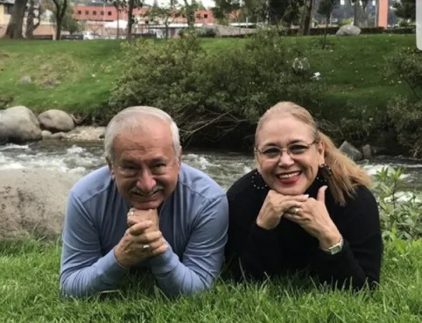 Pareja de adultos mayores sonriendo y recostados sobre el césped junto a un río. Es el Dr. Amalio Martinez Nieto con su esposa Carmen Zea de Martínez.