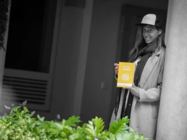 Lucia Toro està parada arrecostada sobre una pared donde muestra su libro Del estrés al SER